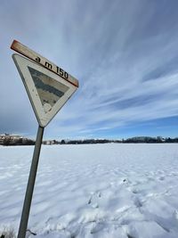 Road sign on snow covered shore against sky