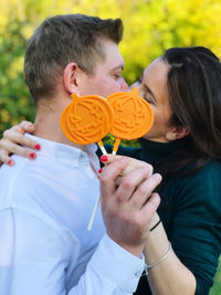 Young couple holding orange candies while kissing outdoors