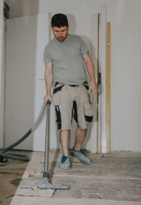 A young man vacuums the floor with a construction vacuum cleaner.