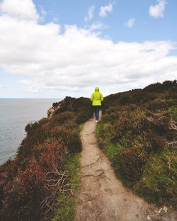 Rear view of person walking on trail by sea against sky