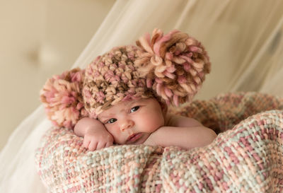 Portrait of cute baby girl wearing knit hat while lying in basket at home