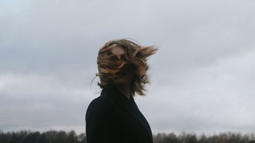 Side view of woman shaking head while standing against sky