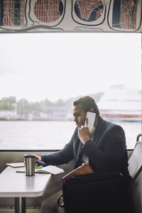 Male freelancer talking on mobile phone while sitting at table in ferry