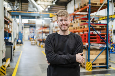 Smiling young employee with arms crossed at factory