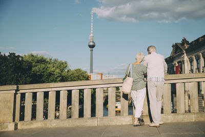 Rear view of senior couple looking at communications tower from bridge in city on sunny day