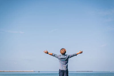 Rear view of man with arms outstretched standing by sea against sky