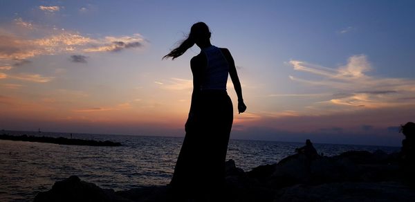 Silhouette people standing on rock by sea against sky during sunset