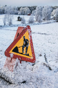 Construction sign covered in snow by a countryside road with winter landscape in the background