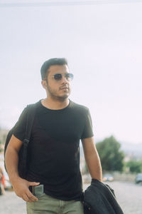Portrait of young man wearing sunglasses standing against sky