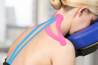 Rear view of mature woman with pink kinesio tape sitting on neck massage chair