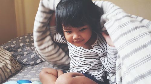 Cute girl with blanket sitting on bed at home