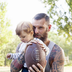 Portrait of bearded man with son holding american football ball 