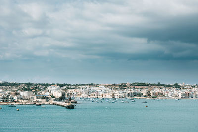 Sailboats in sea by townscape against sky