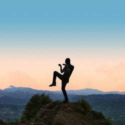 Full length of man standing on rock against sky during sunset