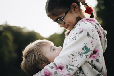 Close-up of siblings embracing against sky