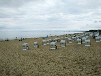 Hooded chairs at beach against cloudy sky