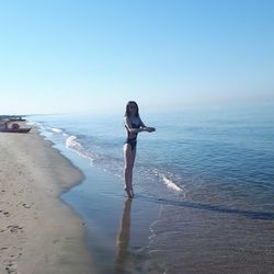 Woman standing on shore at beach against clear sky