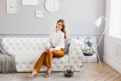 Full length portrait of young woman sitting on floor at home