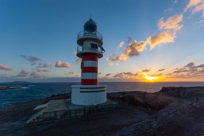 Lighthouse by sea against sky during sunset