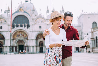 Couple holding map standing against building outdoors