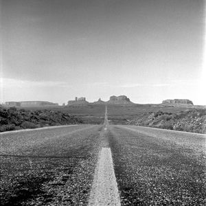 Road by agricultural field against sky