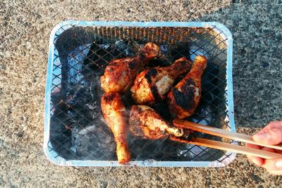 Cropped hand of person grilling meat on metal grate