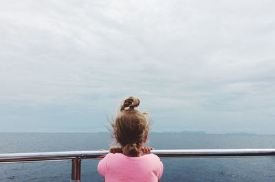 Rear view of girl standing by railing at sea against sky