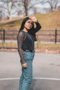 Young woman shielding eyes while standing on road in city