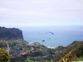 High angle view of person paragliding over sea against cloudy sky