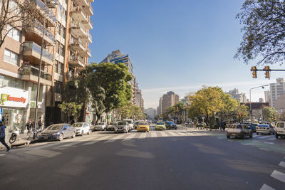 Cars on road by buildings in city against clear sky