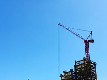 Low angle view of crane against clear blue sky