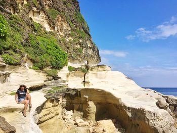 Woman sitting on kapurpurawan rock formation against sky