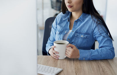 Midsection of woman holding coffee cup on table