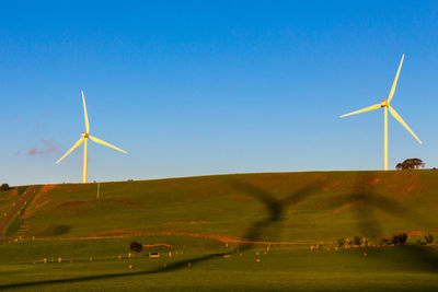 Windmill on field against clear blue sky