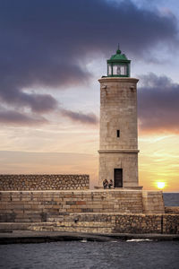 Lighthouse by building against sky during sunset