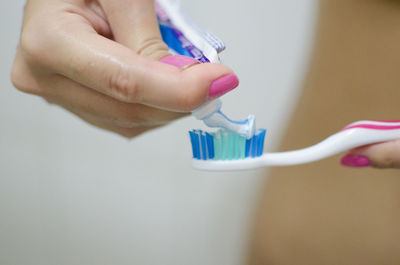 Cropped hand of woman applying toothpaste on toothbrush in home