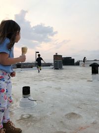 Side view of girl with ice cream cone standing on building terrace against sky