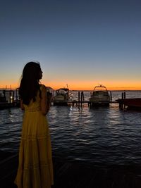 Woman standing on sea against sky during sunset