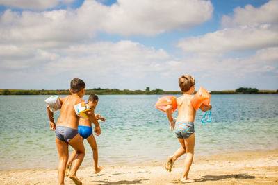 Shirtless boys running at beach against sky