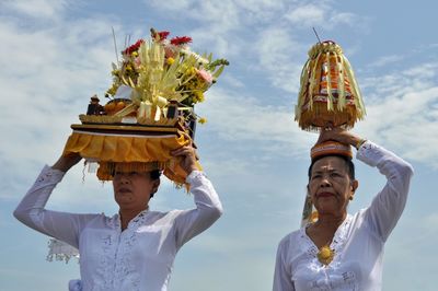 Women carrying religious offerings on head against sky