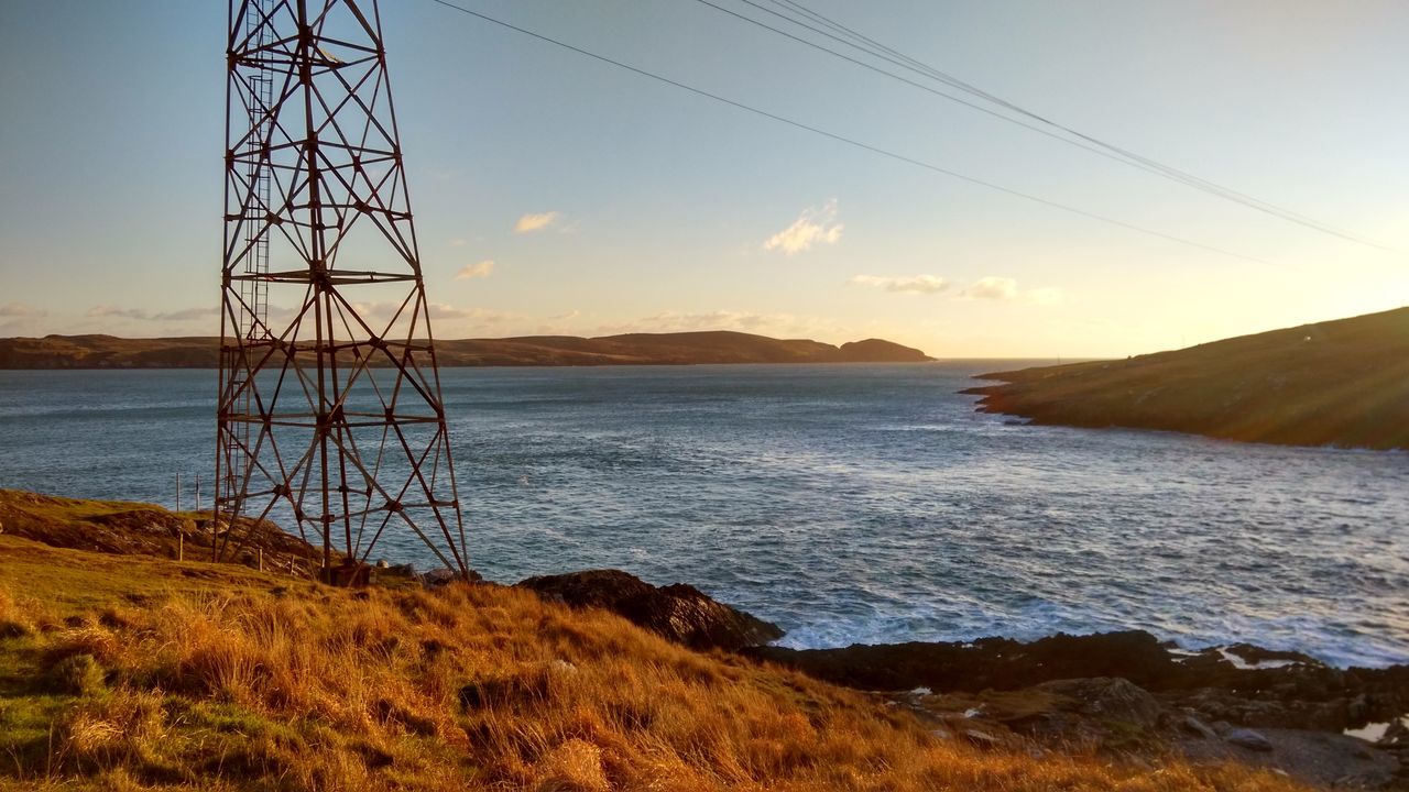 ELECTRICITY PYLON BY SEA AGAINST SKY