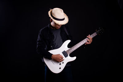 Midsection of man playing guitar against black background