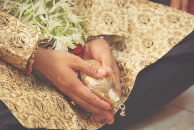 Midsection of groom with jewelry sitting on floor during wedding ceremony