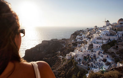 Woman from behind watching the sunset at oia town in santorini island.