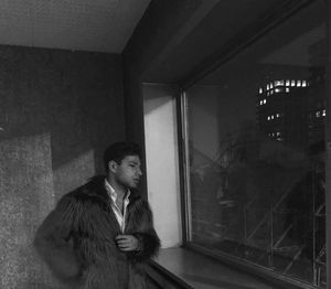 Man wearing warm clothing while looking through window