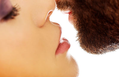 Close-up of woman kissing bearded man over white background