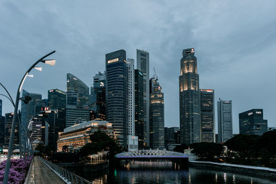 Modern buildings by river against sky in city