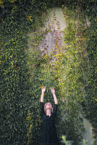 Woman standing with arms raised against ivy