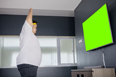 Side view of man with arms raised looking at lcd screen at home