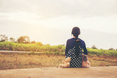 Rear view of woman sitting on field against sky